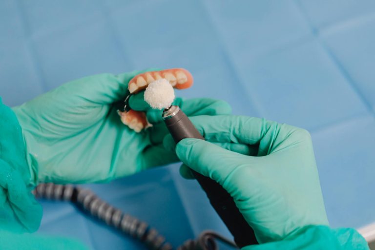 Close-up of a dental technician polishing a denture with precision tools and surgical gloves.