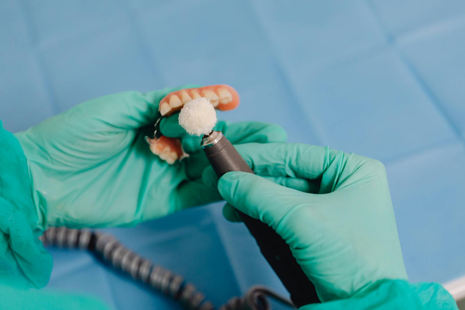 Close-up of a dental technician polishing a denture with precision tools and surgical gloves.